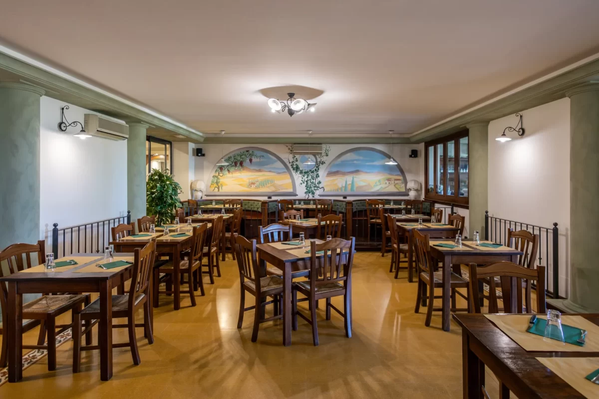 Interno di una sala ristorante con tavoli in legno e dipinti murali.