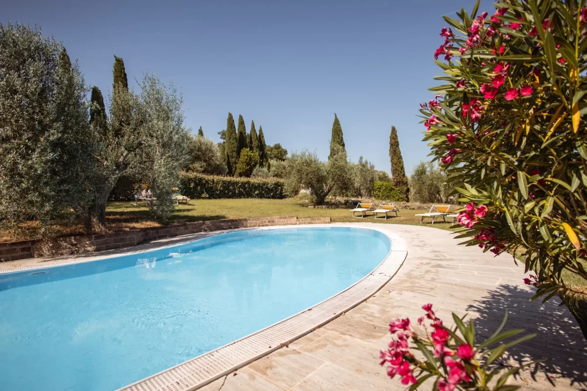 Piscina all'aperto circondata da giardino con cipressi e oleandri fioriti.